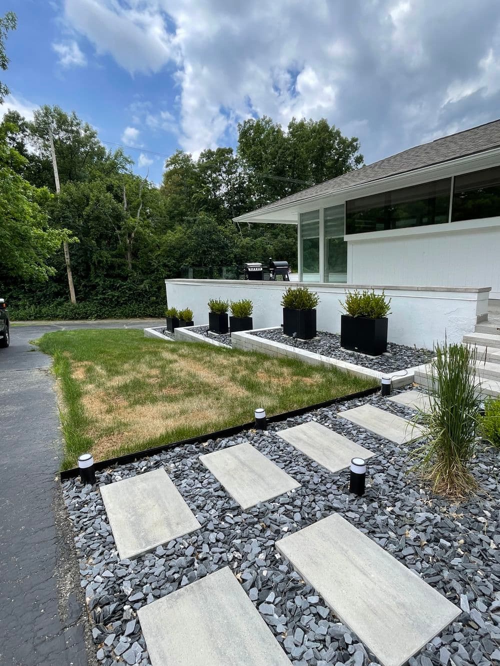 Modern front yard landscaping with stone pathway, gravel, and potted plants near a house.