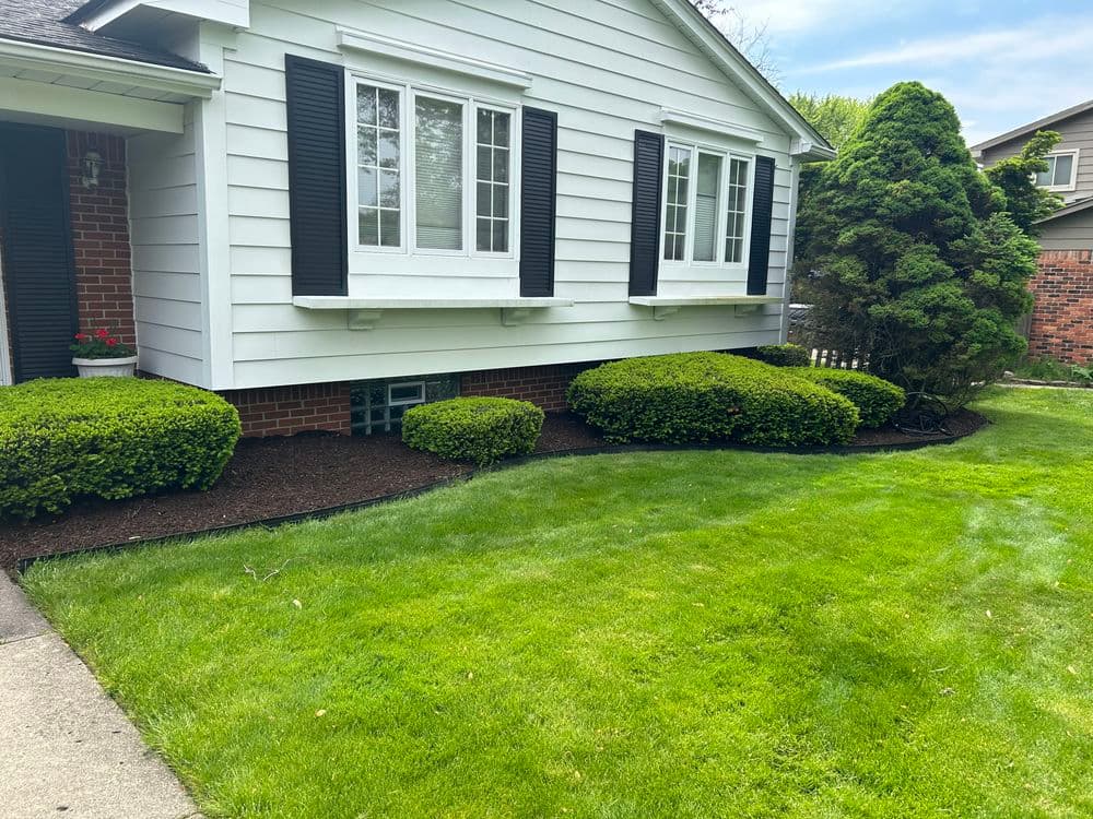 Well-maintained house exterior with shrubs, manicured lawn, and freshly mulched flower beds.
