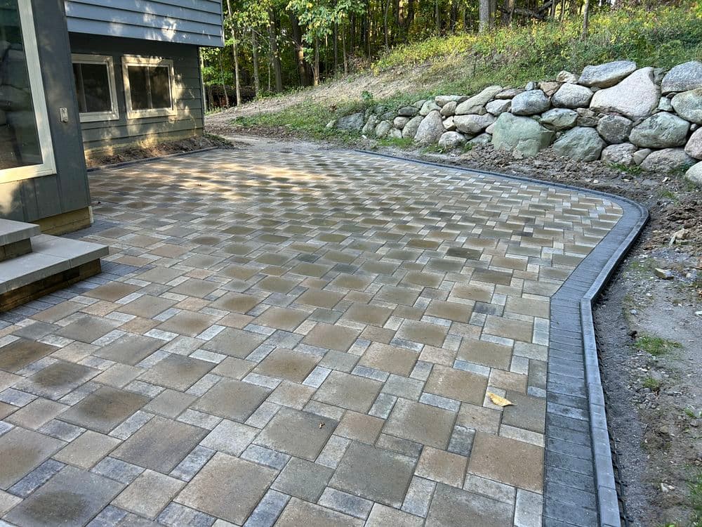 Paved stone patio installation with curved edge and surrounded by greenery and rocks.