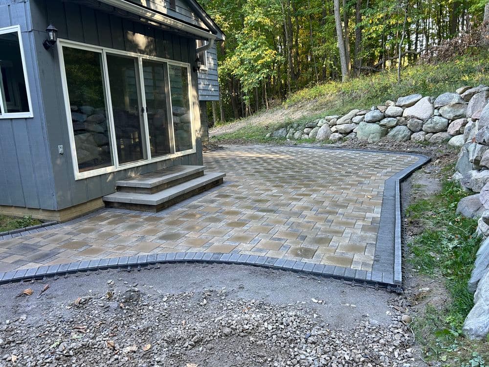 Paved patio area with steps, flanked by stone wall and surrounded by trees. Perfect outdoor space.