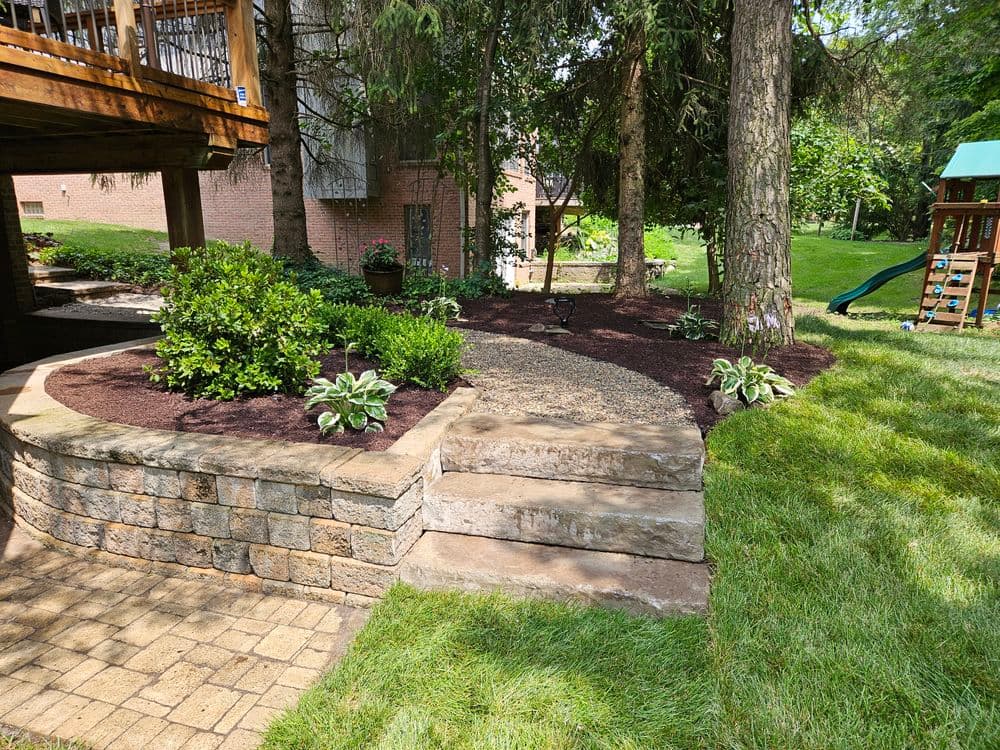 Landscaped garden with stone steps, greenery, and a playset under trees.