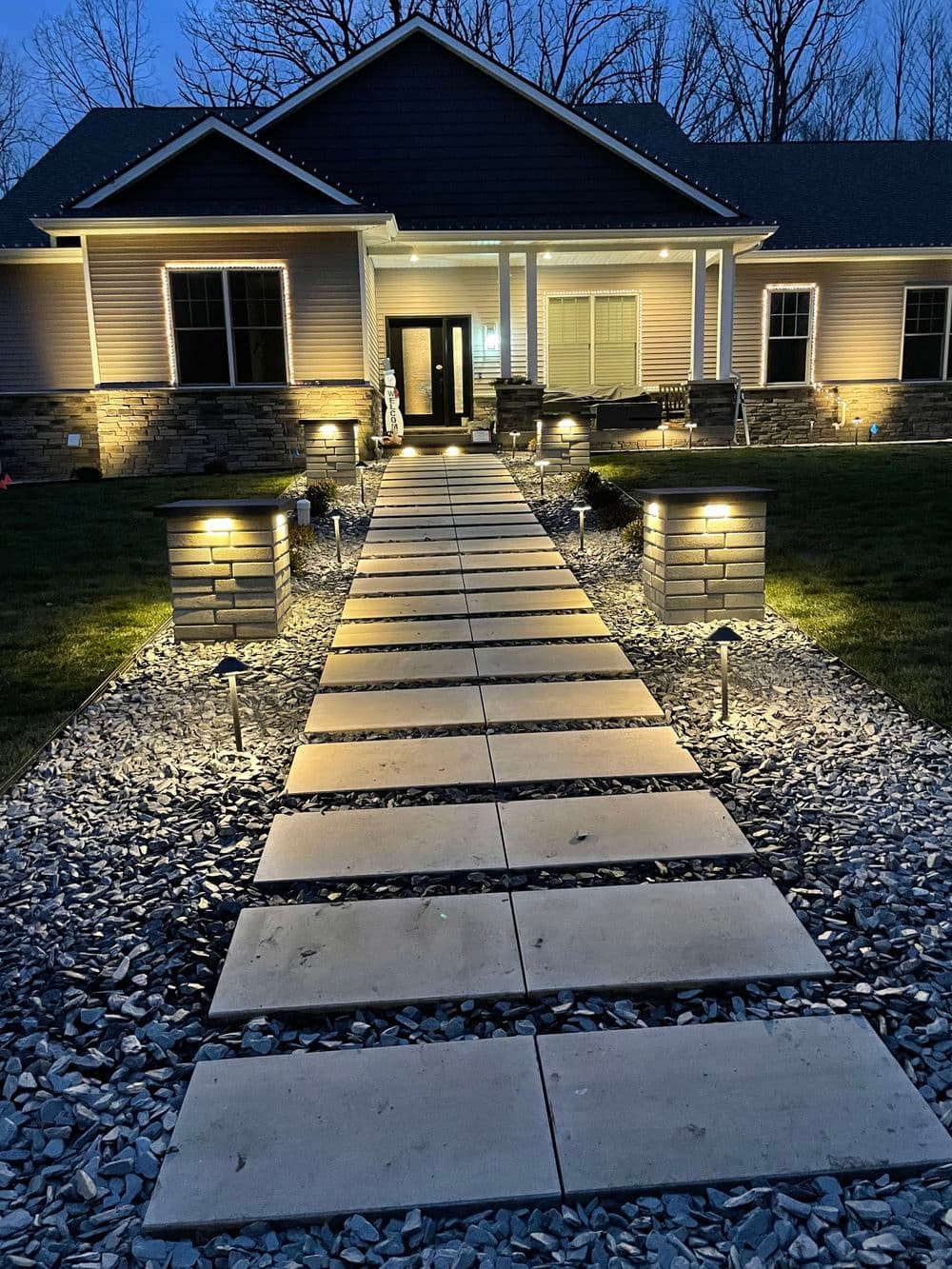 Well-lit stone path leading to a modern home entrance at dusk, surrounded by landscaped gardens.