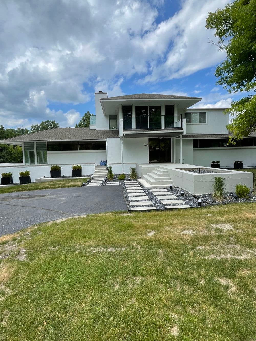 Modern white house with large windows, landscaped yard, and stone pathway under a cloudy sky.