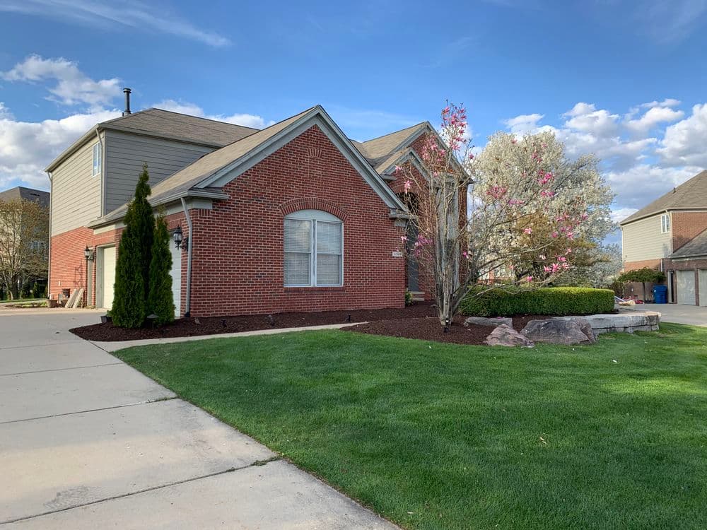 Beautiful brick house with landscaped yard, flowering tree, and clear blue sky.