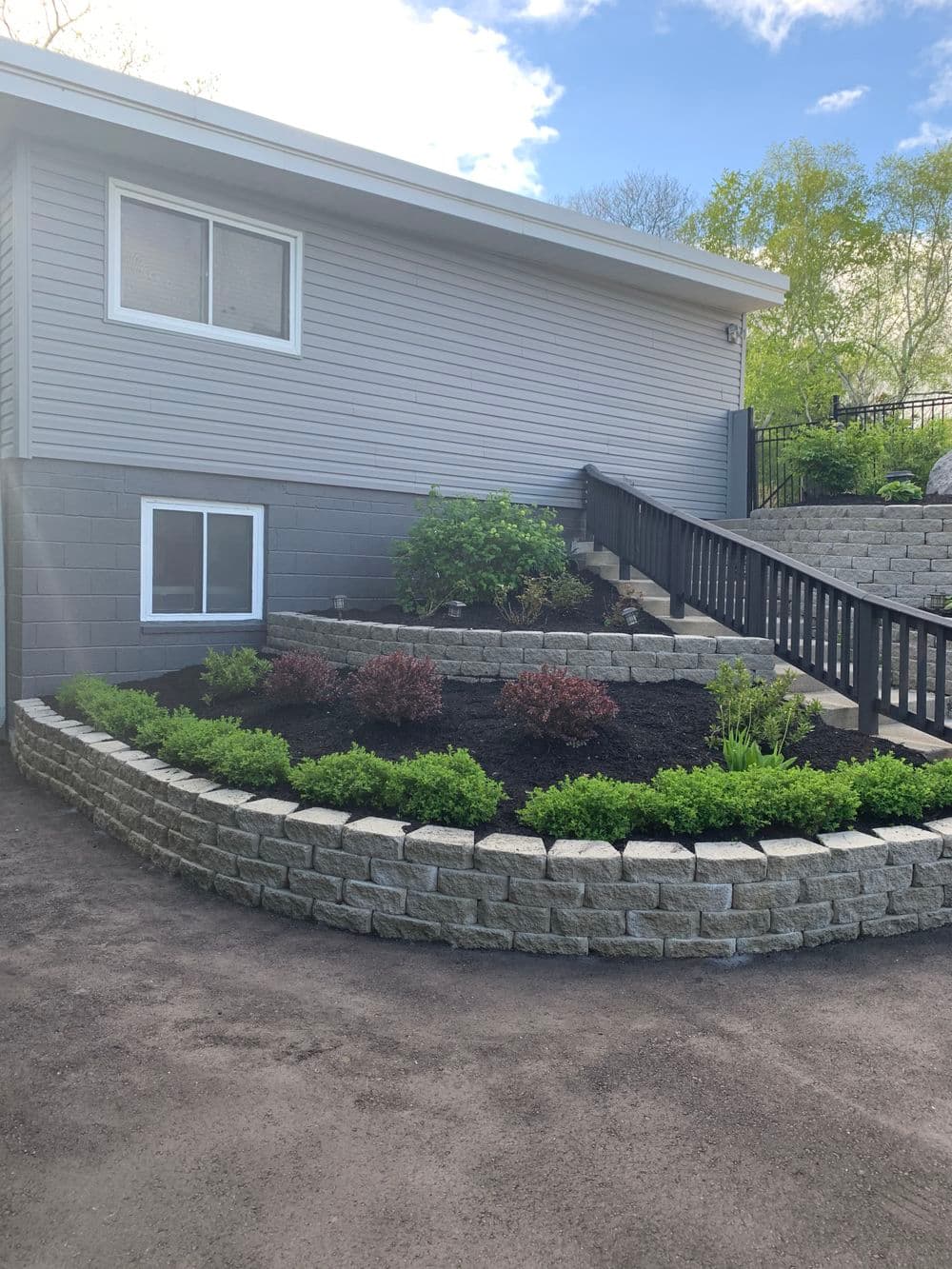 Modern home exterior with landscaped garden featuring stone retaining wall and vibrant greenery.