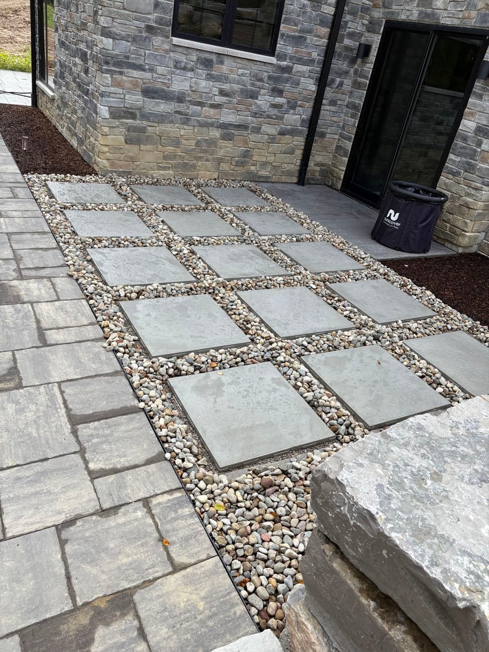 Modern stone patio design featuring concrete pavers and decorative gravel landscaping.