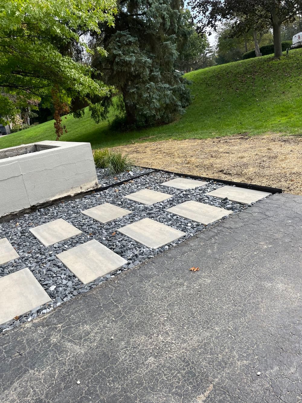 Stone pathway with gravel accents in landscaped yard featuring greenery and trees.