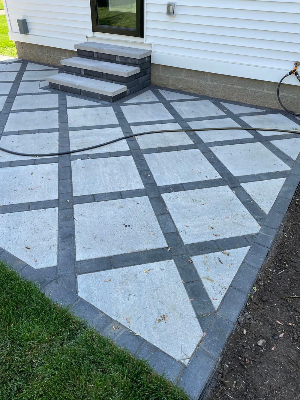 Enhanced patio with gray stone pavers and decorative border, leading to steps and lawn.