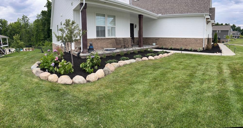 Lush landscaping with rocks and flowers by a modern home in a green lawn setting.