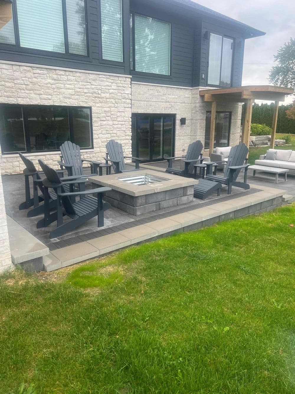 Modern outdoor sitting area with Adirondack chairs and fire pit beside a home.