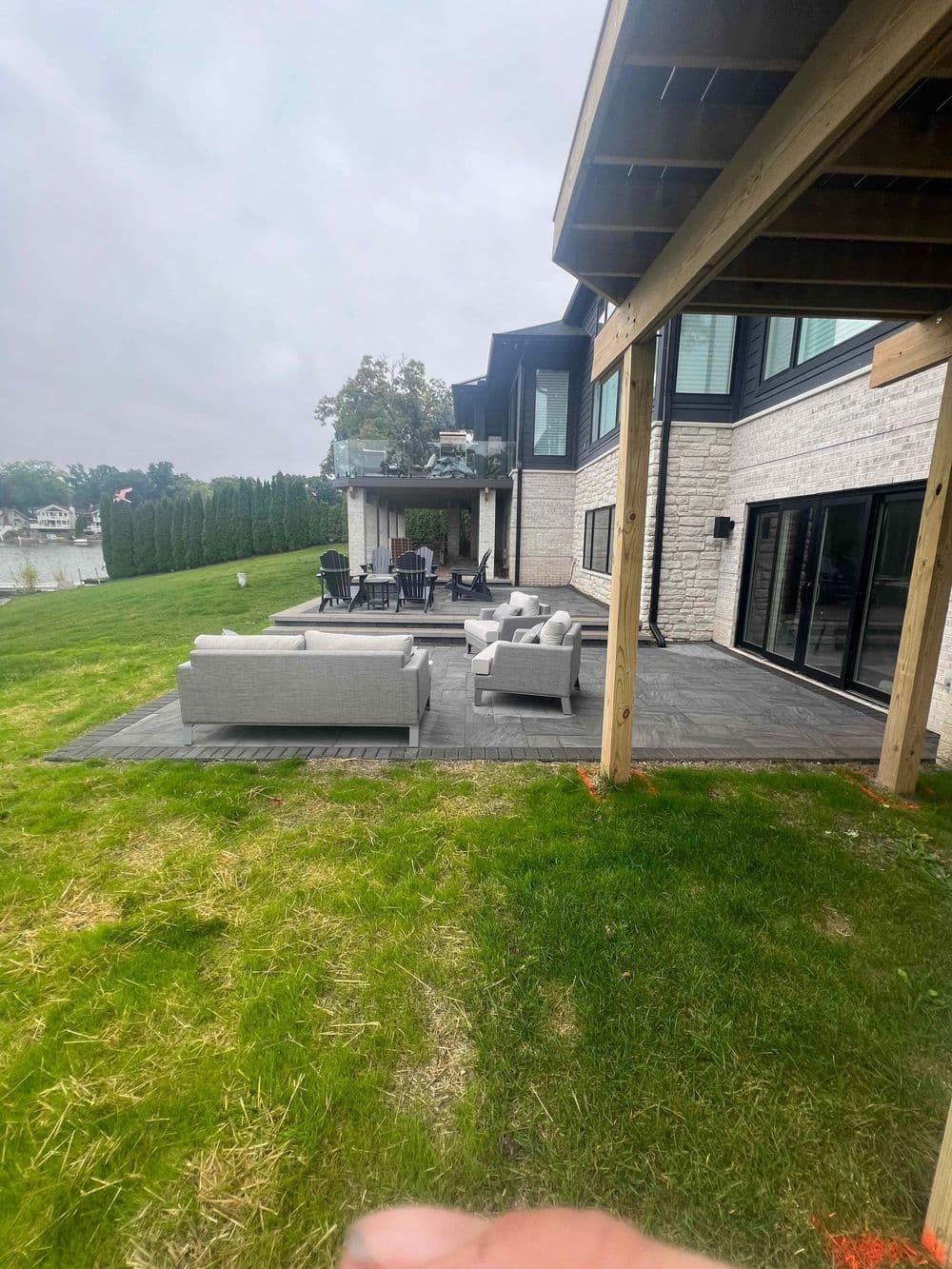 Modern lakeside home with outdoor seating area and patio overlooking lush grass.