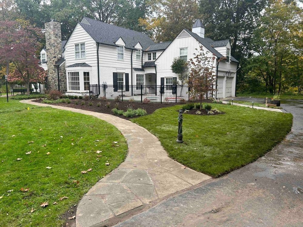 Elegant white house with black accents, landscaped garden, and winding stone walkway.