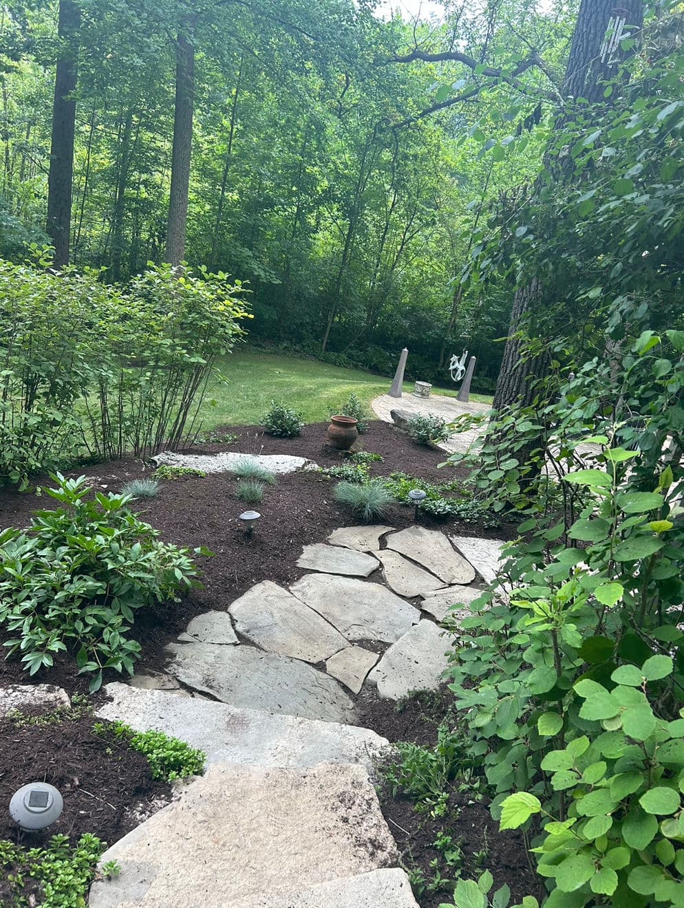 Natural stone pathway winding through a lush garden with greenery and sculpture in the background.